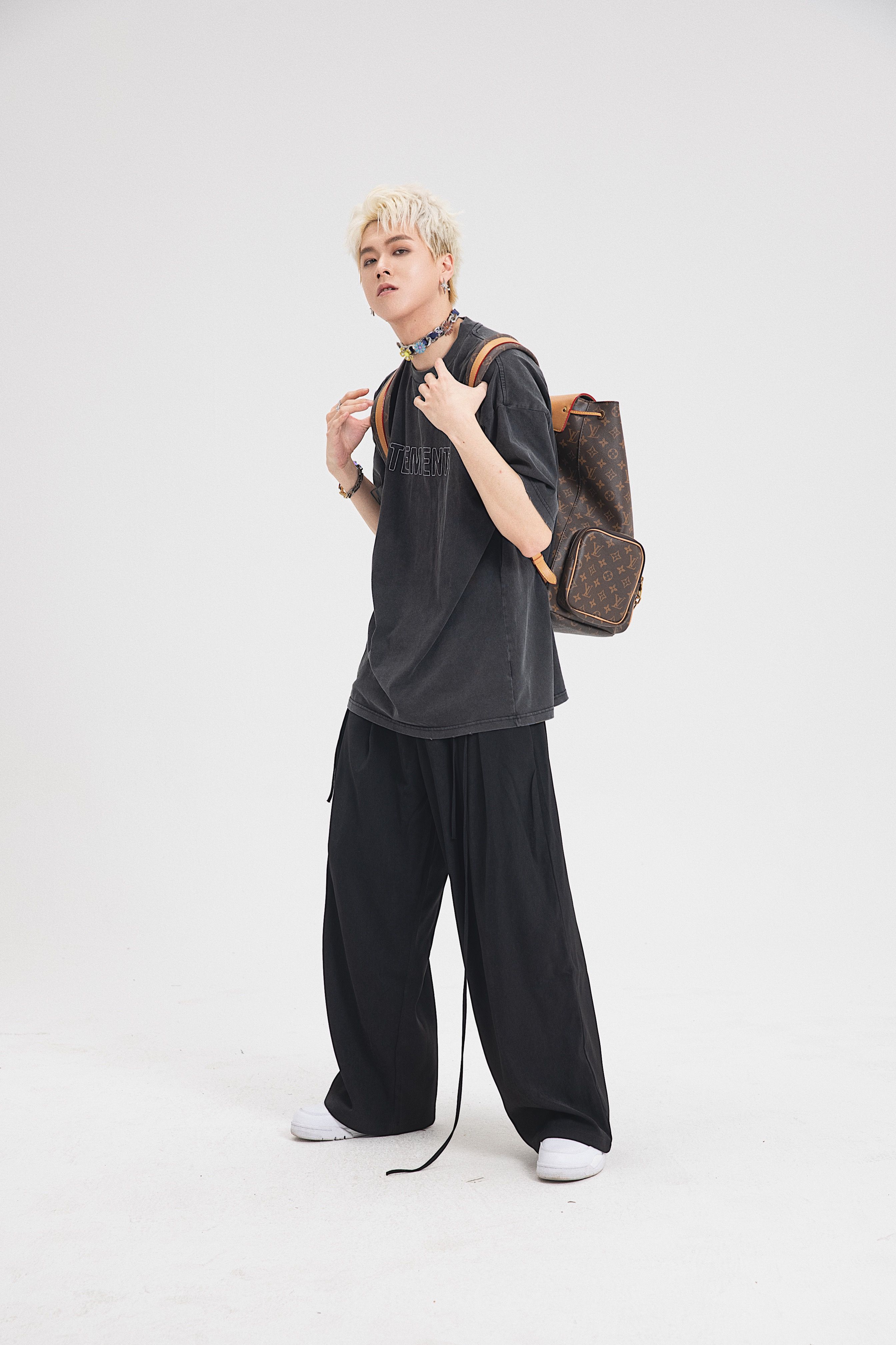 Stylish young adult with dyed hair and backpack in a studio shot, wearing fashionable streetwear.