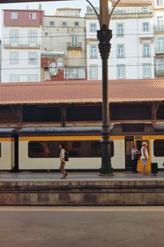 People waiting and walking by a train at an urban railway station platform.