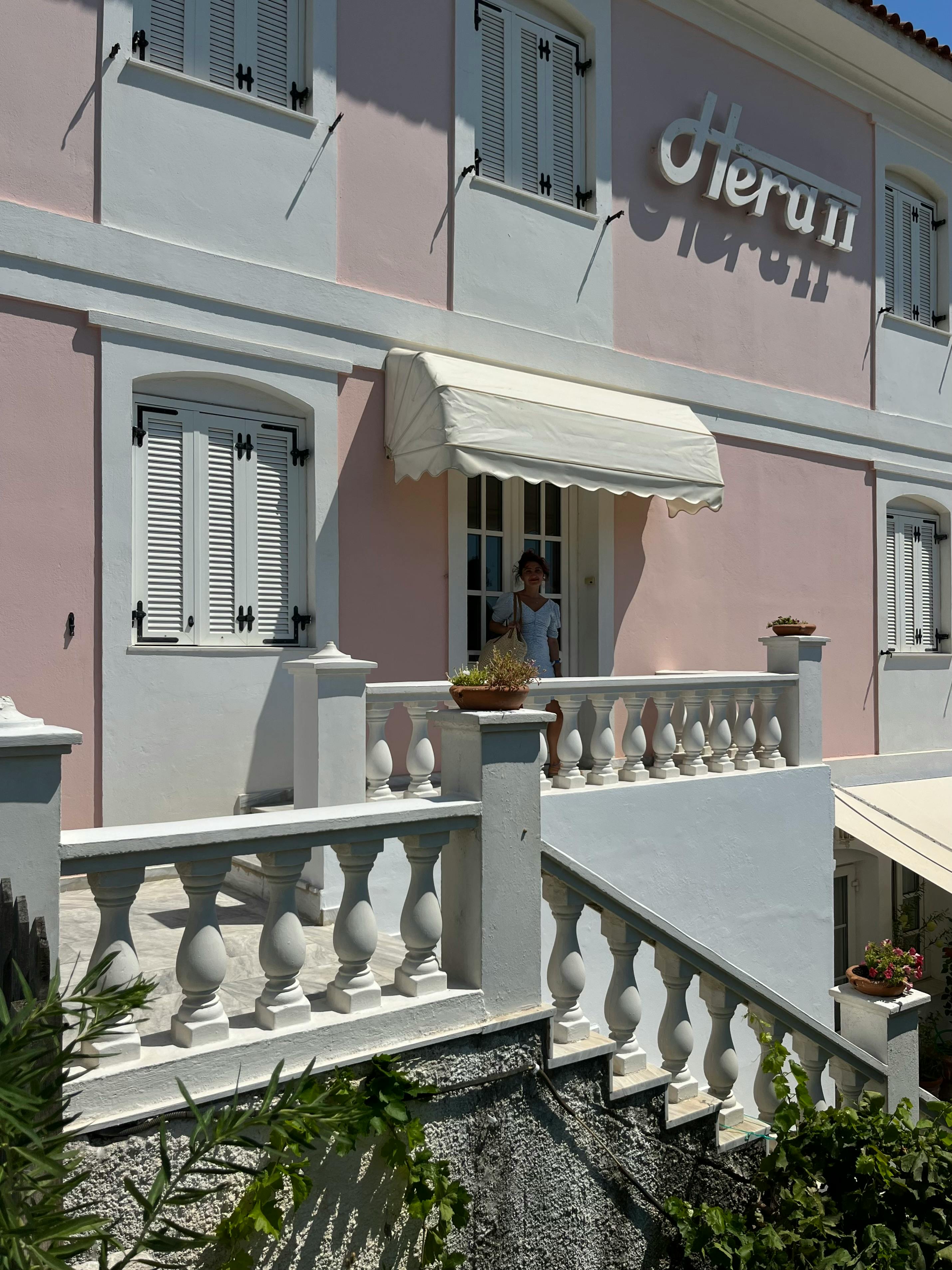 Elegant facade of Hotel Hera II in Samos with woman standing on balcony.