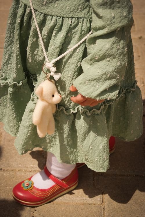 Free Adorable toddler in a green dress with a teddy bear pendant and red shoes in İstanbul. Stock Photo
