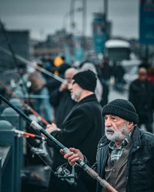 Free Senior man fishing on a bustling Istanbul bridge, enjoying a leisurely pastime. Stock Photo