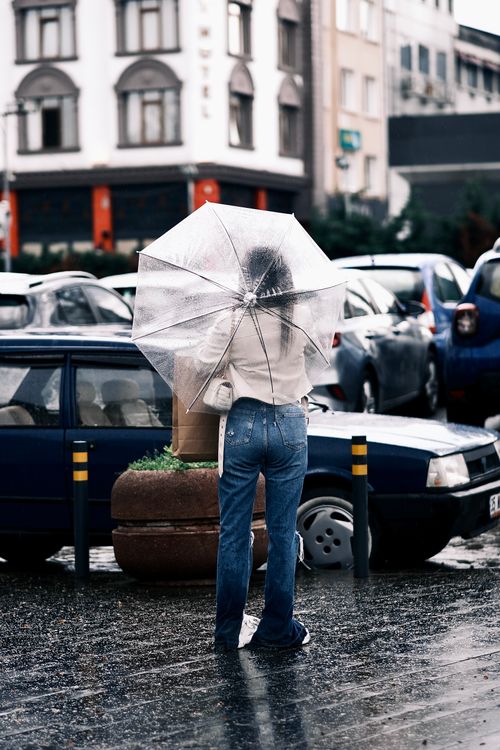 Free A woman stands in a rainy city street holding a transparent umbrella. Stock Photo