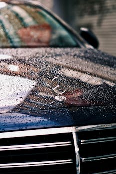 Wet car hood with visible logo and raindrops, showcasing automotive design and texture.
