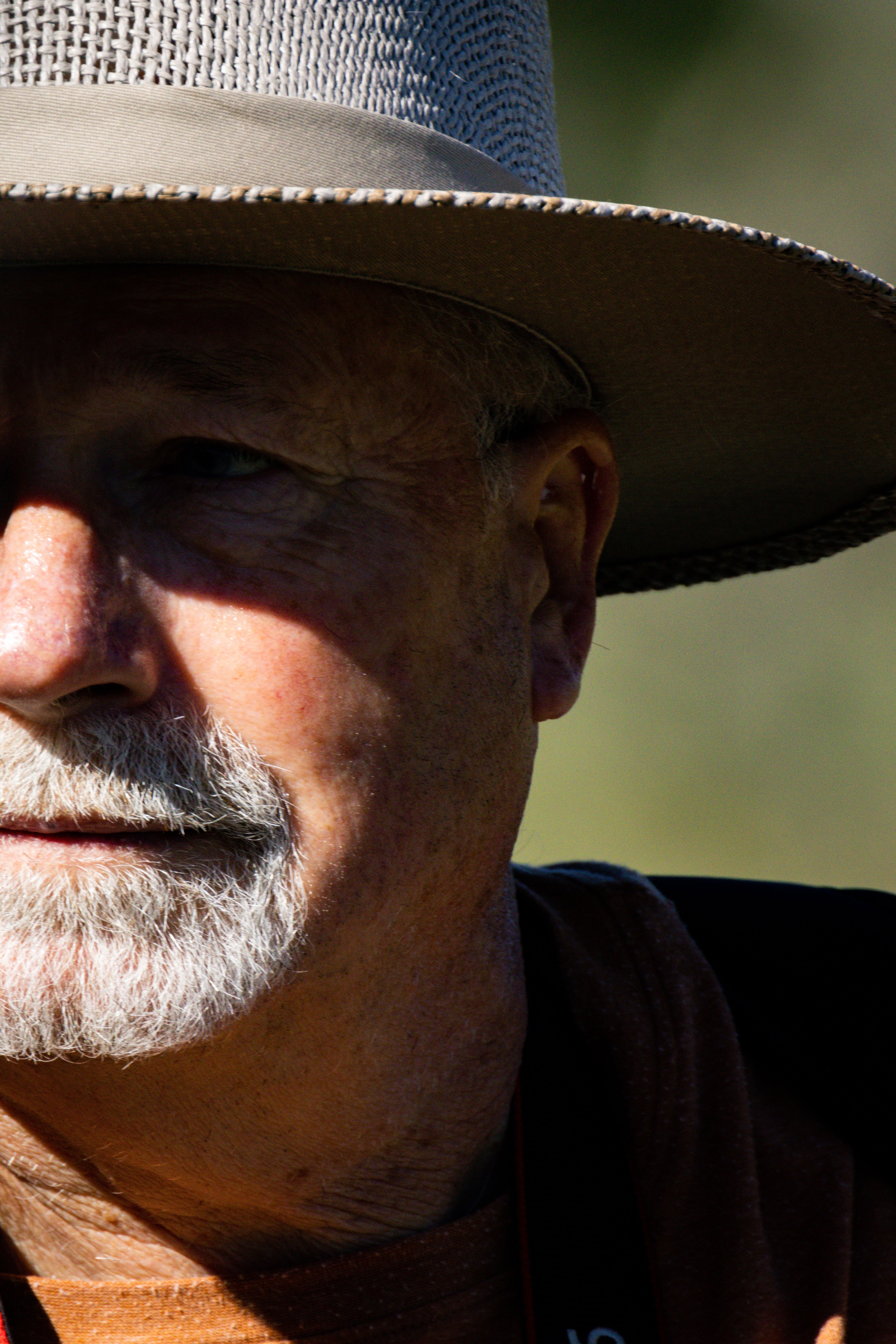 A close-up, shadowed portrait of an elderly man with a beard and hat in natural lighting.