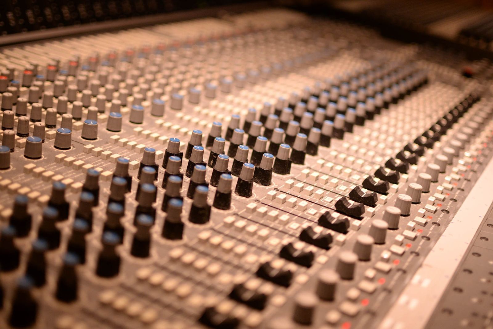 Analog audio mixing console with knobs and sliders in dim studio lighting