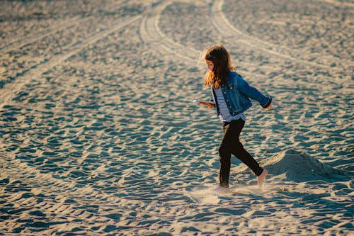 Girl in Jacket Walking with Cellphone on Beach