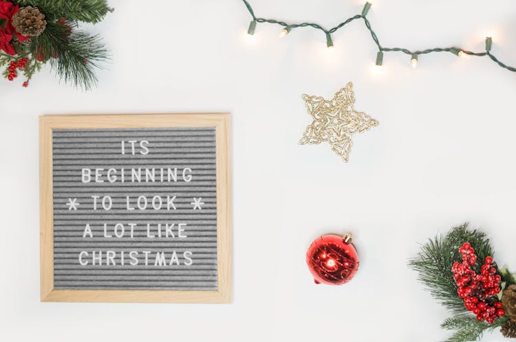 It's Beginning To Look A Lot Like Christmas Board Decor Beside Star And Red Bauble Flatlay Photography