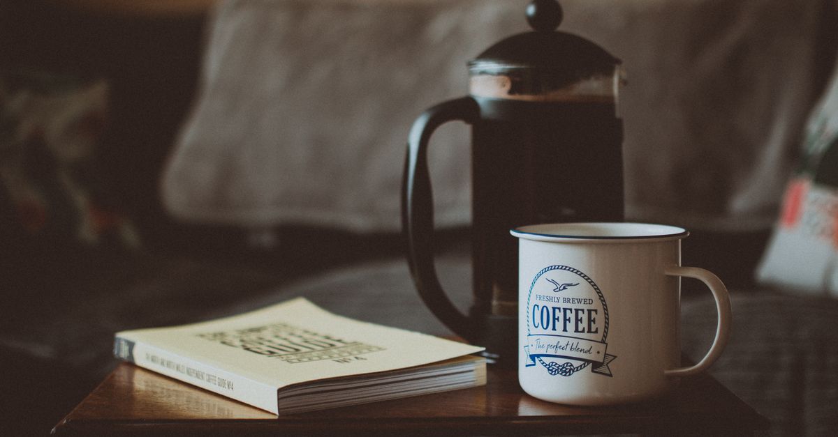 A cozy living room with a steaming mug of tea, soft sunlight streaming through a window, and an open book on a wooden table — no phones in sight