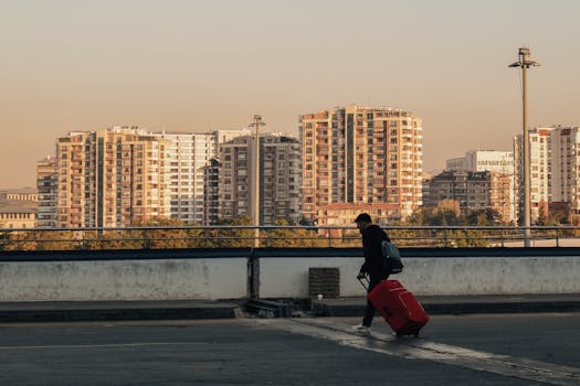 Silhouette of a person with a red suitcase against a city skyline at sunset.