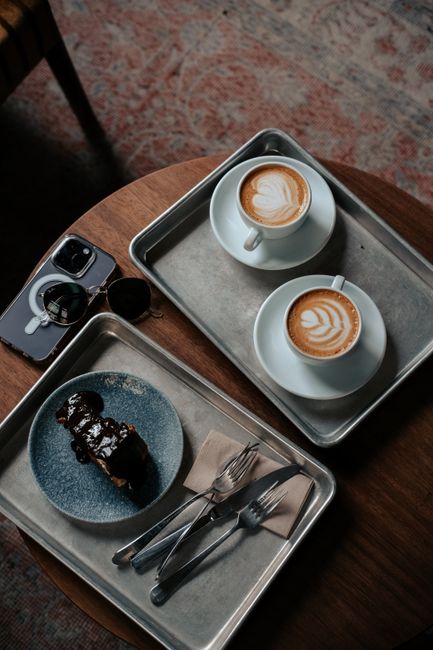 Top view of lattes and pastry on trays in a cozy cafe setting, ideal for coffee lovers.