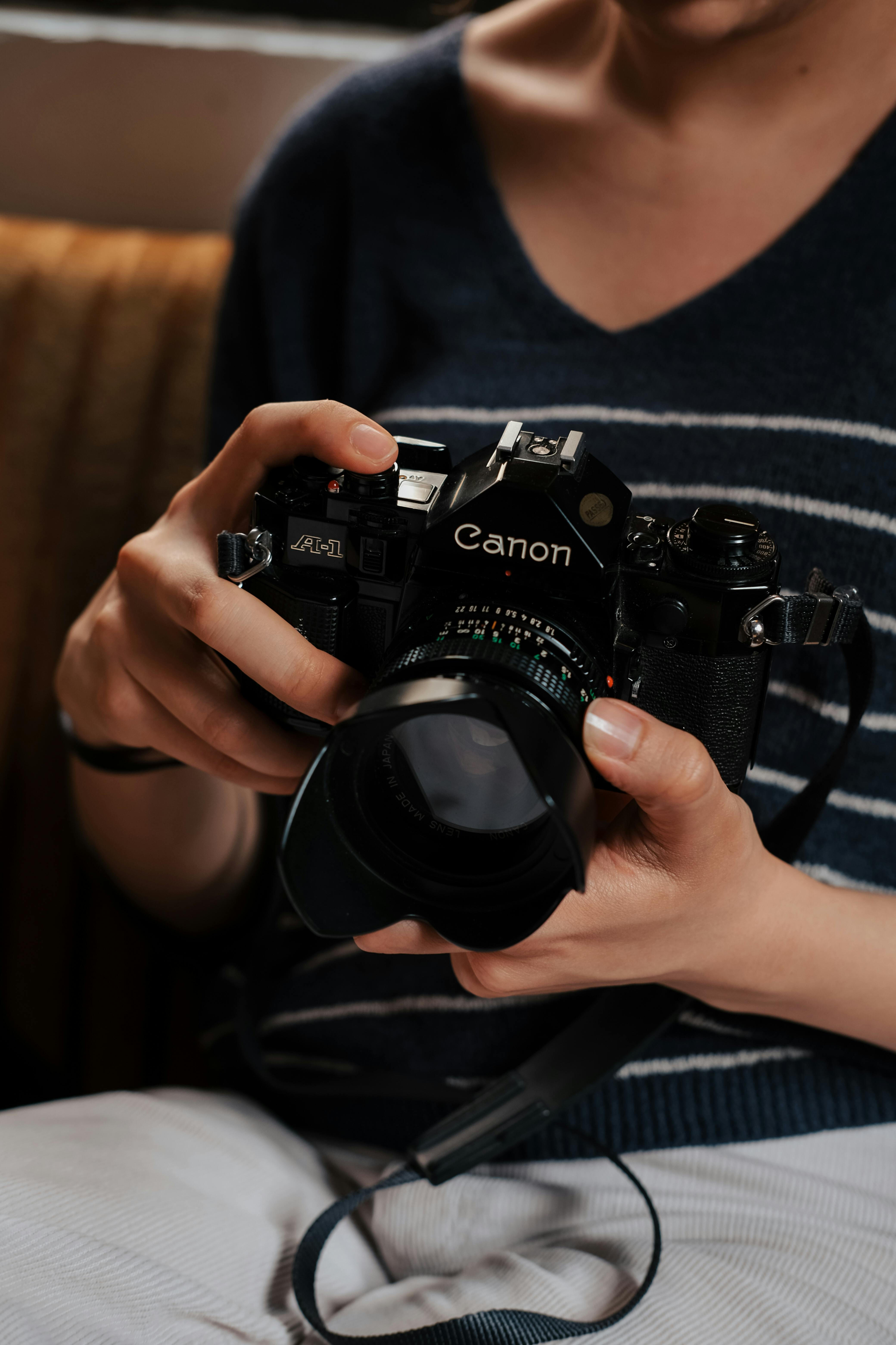 Close-up of hands holding a classic Canon film camera indoors.