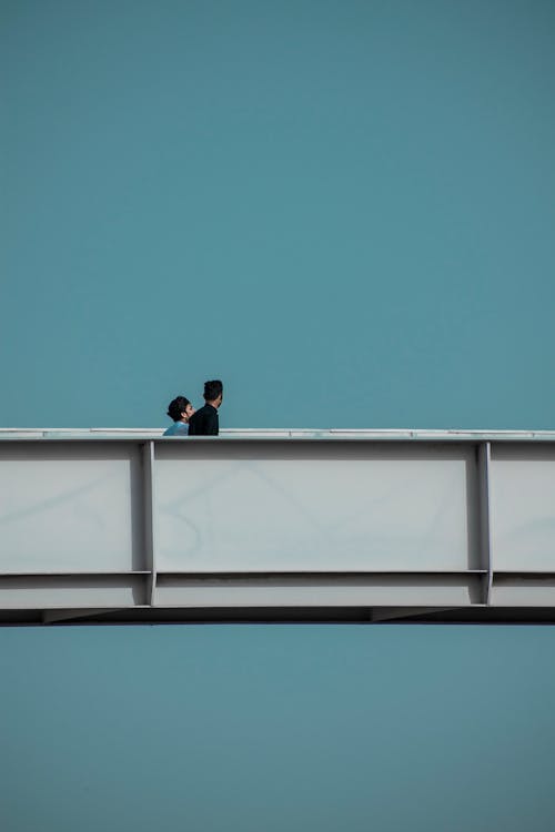 Two Men Crossing an Elevated Walkway Stretching across a Clear Sky