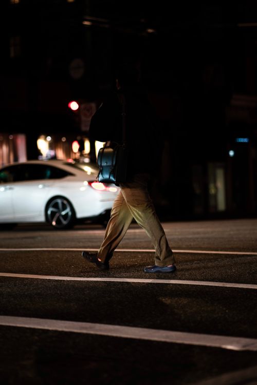 Free A person walks across a city street at night, with a car visible in the background, capturing urban nightlife. Stock Photo
