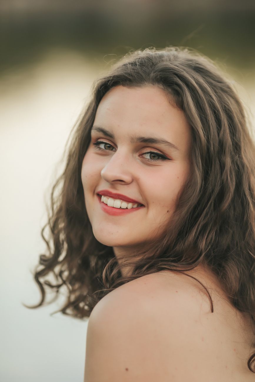 Portrait of a young woman with wavy hair and red lips smiling outdoors.