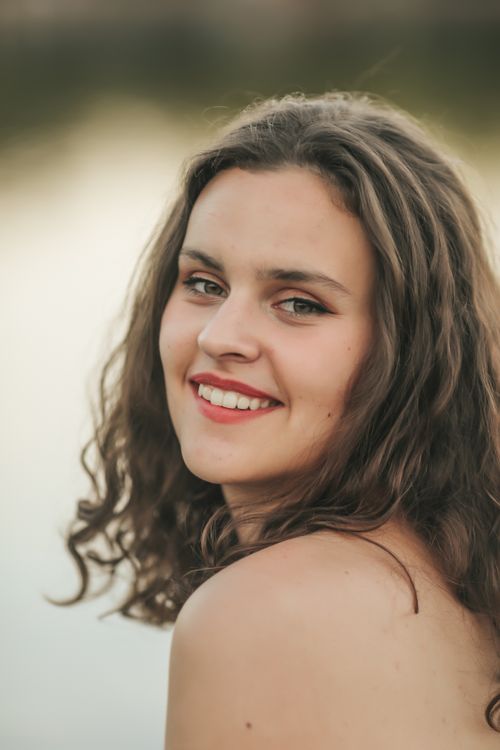 Free Portrait of a young woman with wavy hair and red lips smiling outdoors. Stock Photo