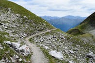 在多云的天空下，一条小路蜿蜒穿过岩石遍布、郁郁葱葱的绿色山地景观