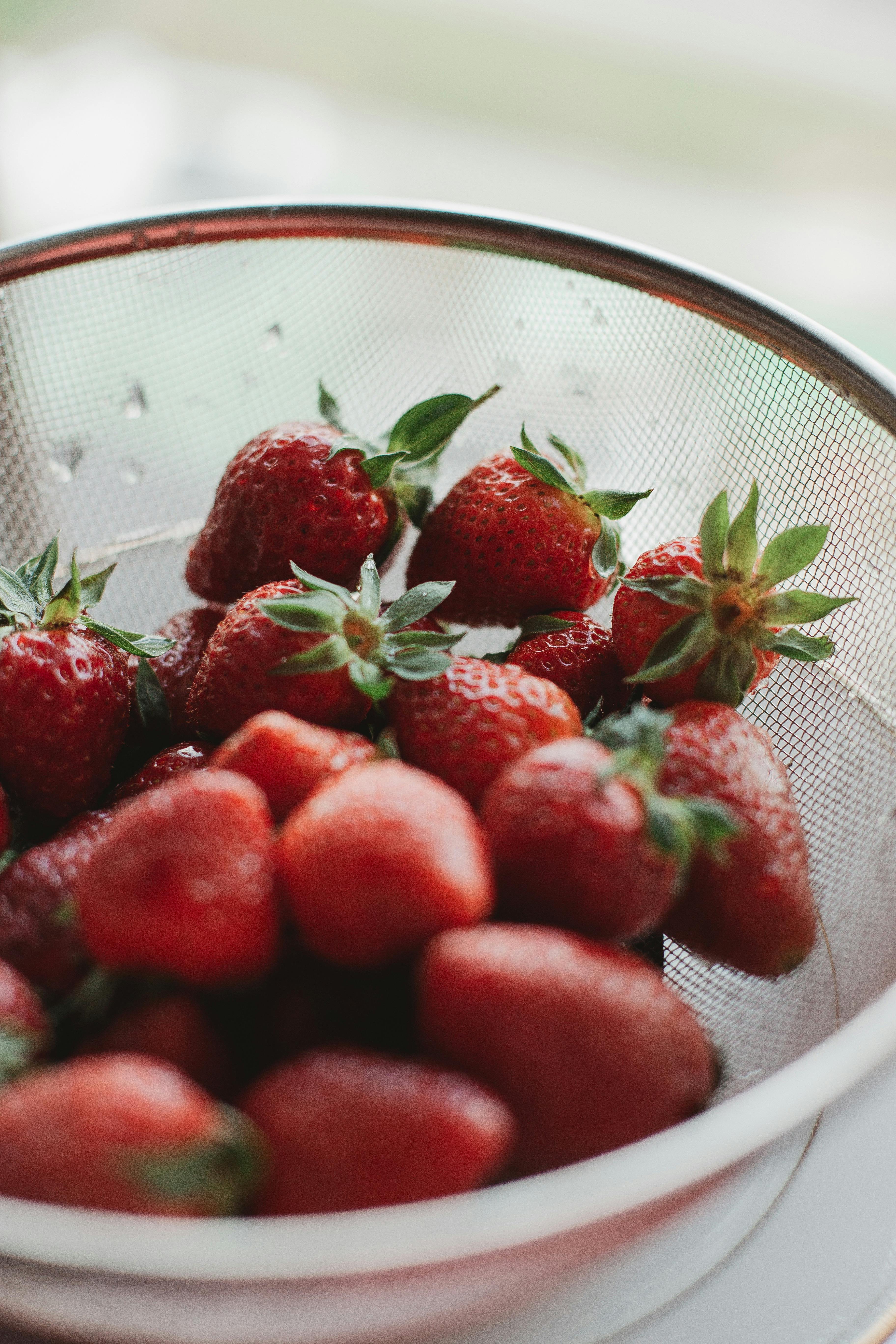 A vertical close-up of fresh strawberries in a metal colander, highlighting their vibrant color.