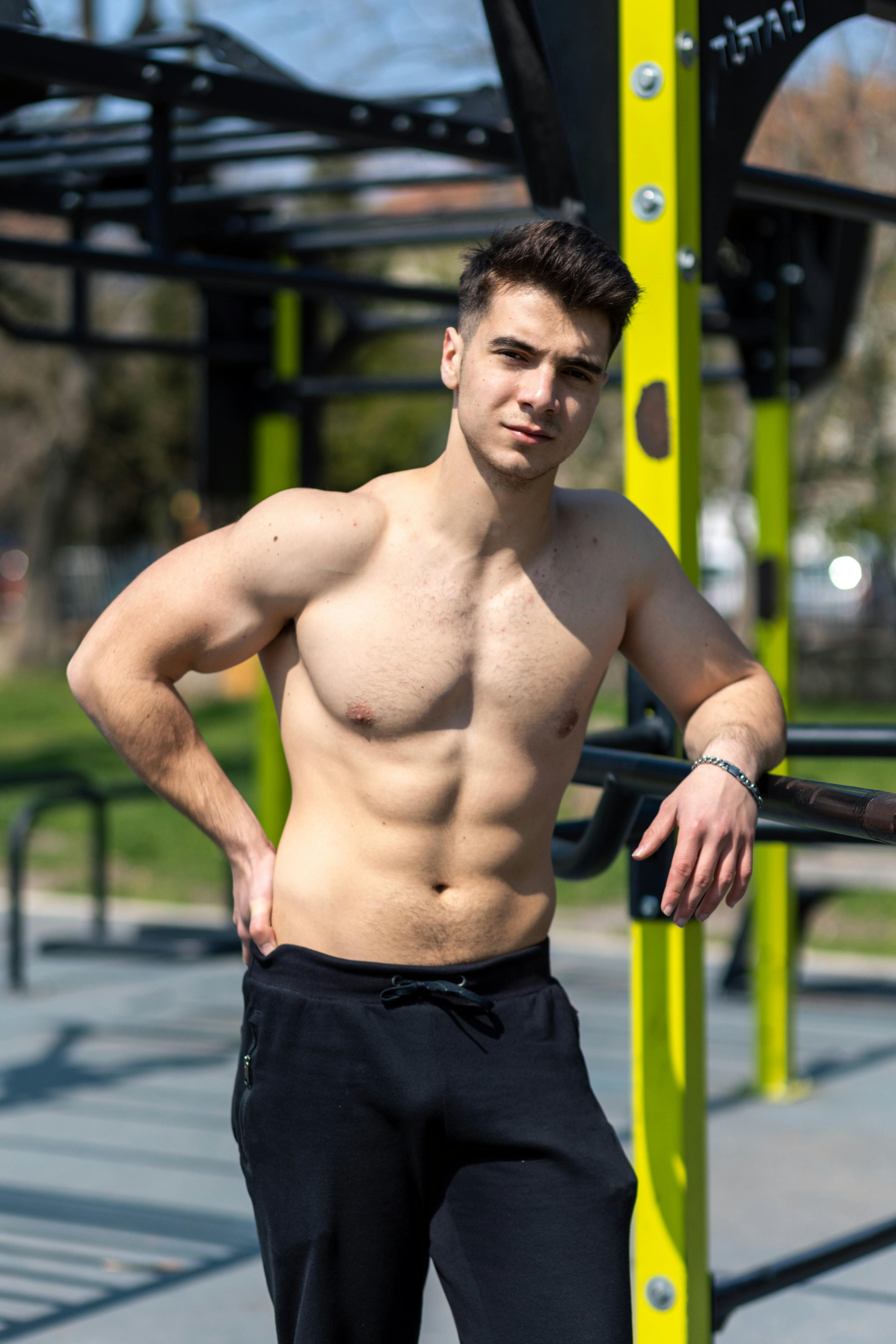 A fit young man working out shirtless at an outdoor gym, showcasing strength and fitness.