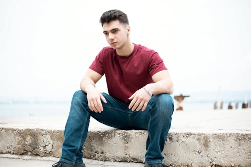 Young Man in a Casual Outfit Sitting on the Shore 