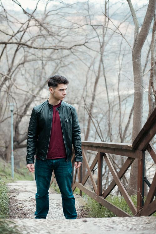 Free Young man in leather jacket posing by railing in natural setting. Stock Photo