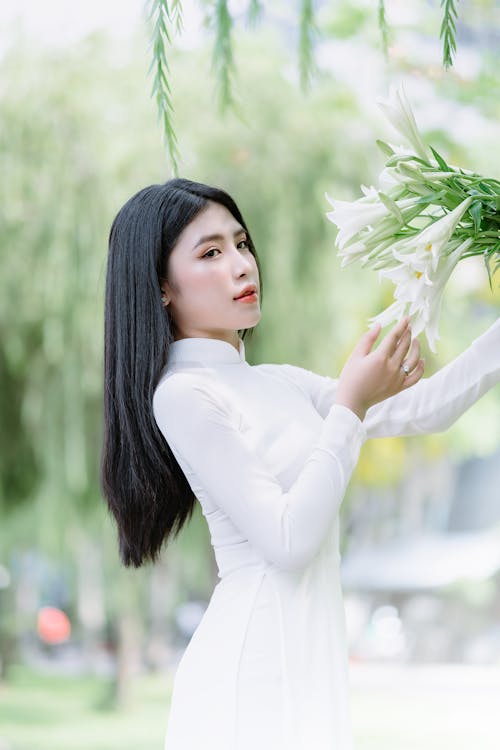 Young Woman in a White Dress Holding a Bouquet of White Lilies 