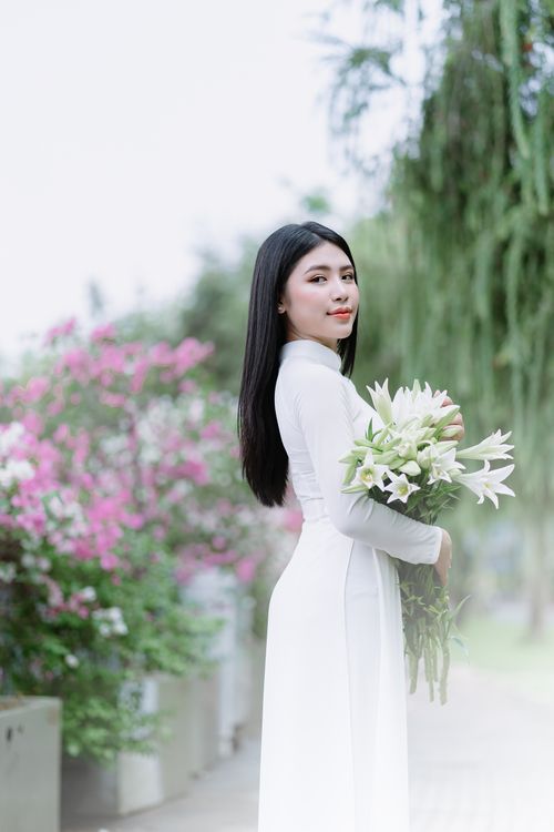 Free Young Asian woman in white dress holding a bouquet of white lilies in a blooming garden. Stock Photo