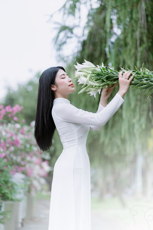 Free Side profile of a woman with long black hair holding a lily bouquet in a serene outdoor setting. Stock Photo