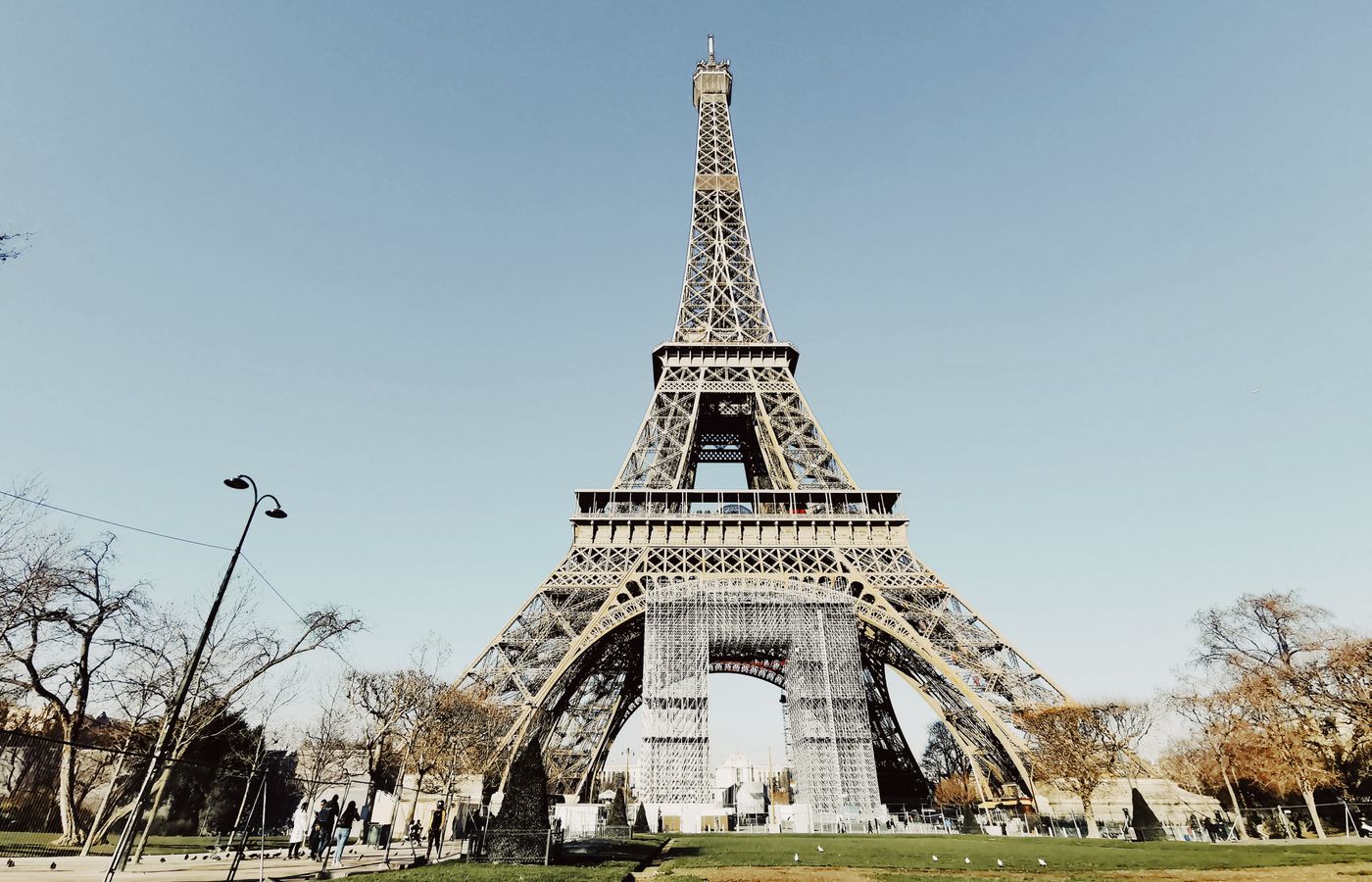 Low angle shot of the Eiffel Tower in Paris with blue sky and partial park view.