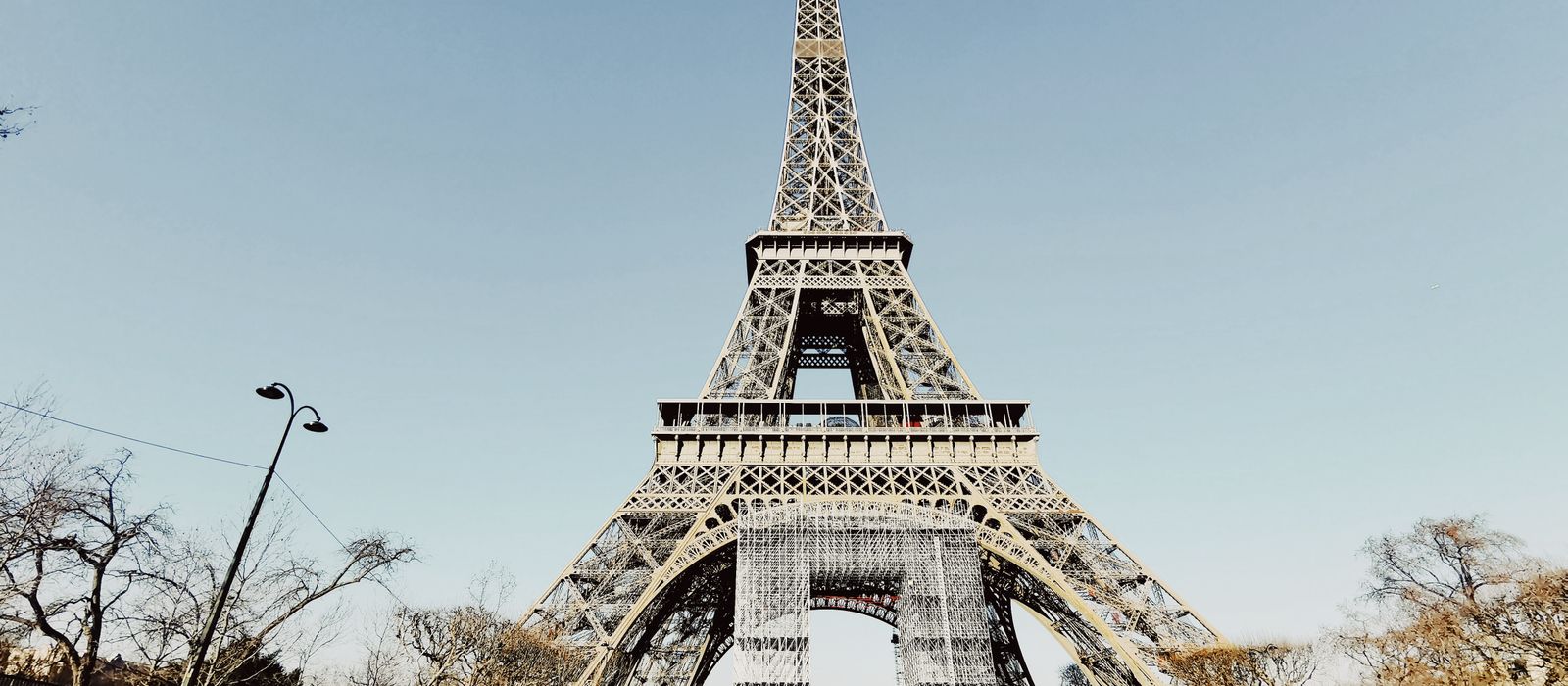 Low angle shot of the Eiffel Tower in Paris with blue sky and partial park view.