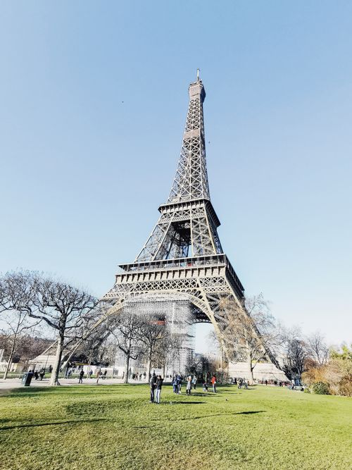 Free A low angle view of the Eiffel Tower in Paris against a clear blue sky with a park setting. Stock Photo
