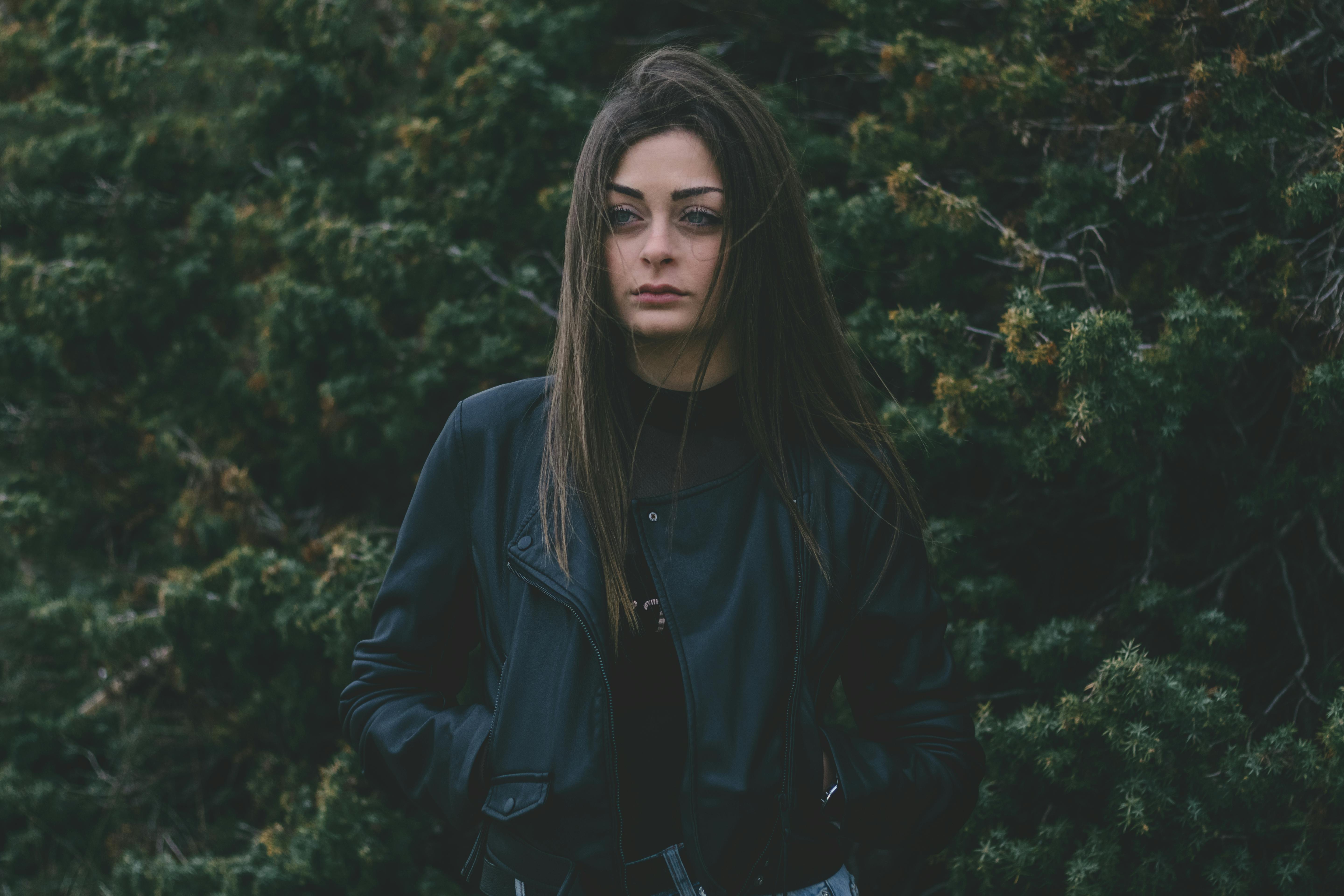一名女子穿着皮夹克，站在郁郁葱葱的绿色背景前，散发着神秘的气息