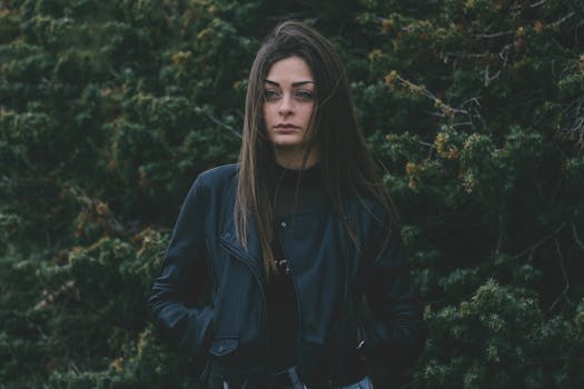 一名女子穿着皮夹克，站在郁郁葱葱的绿色背景前，散发着神秘的气息