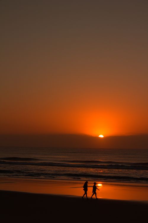 Free Two people walking on Guaratuba Beach during a stunning sunset, creating beautiful silhouettes. Stock Photo
