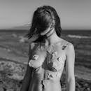 在黑白海滩背景下，一位裸体女性手持纸片