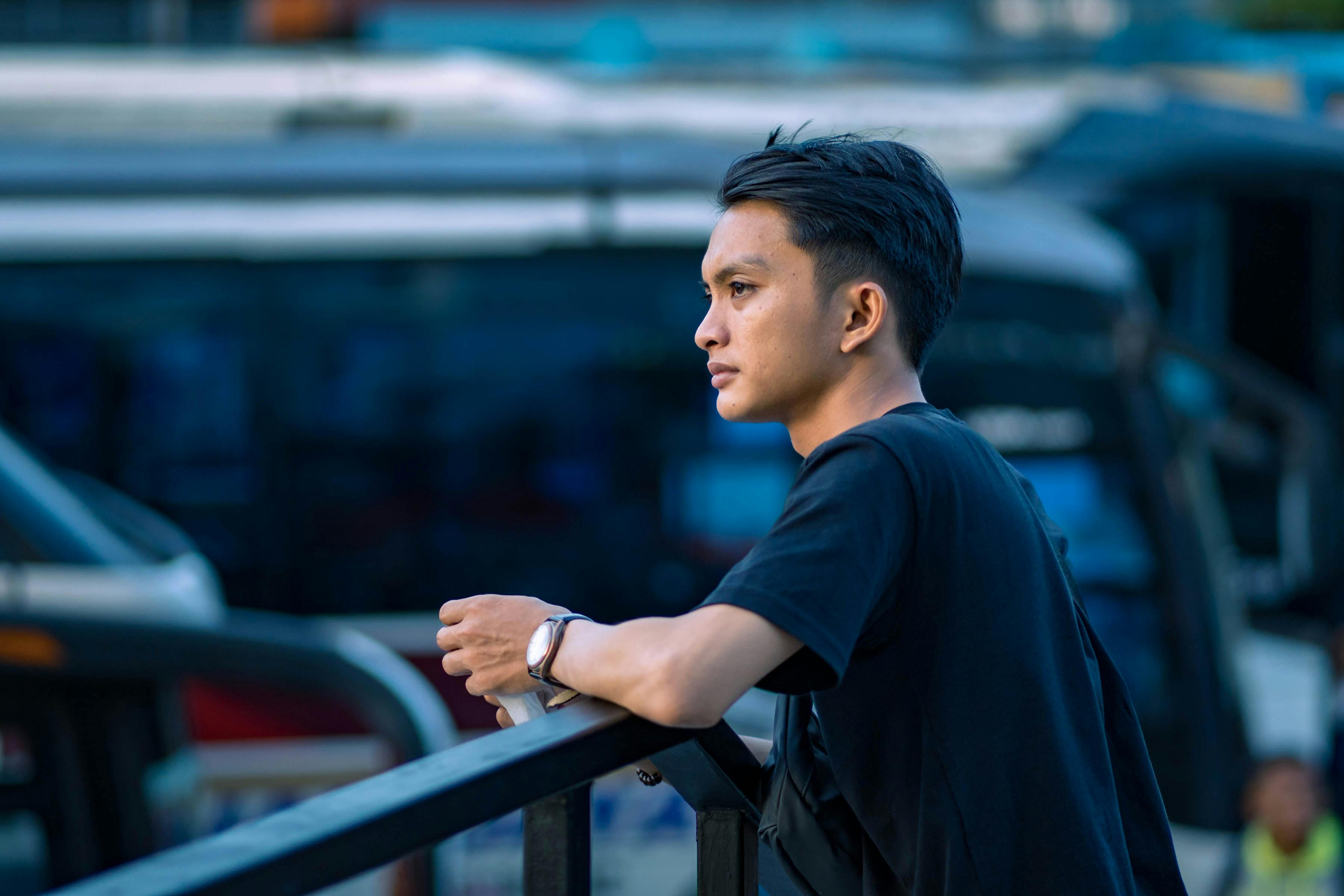 A young man leans on a railing, contemplating in an urban environment.