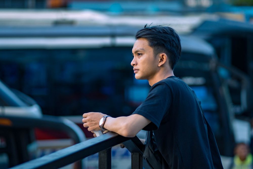 Người đàn ông trẻ châu Á đứng tựa lan can, nhìn xa suy nghĩ