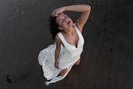 一位身着白色连衣裙的女子宁静地跪在海滩上，尽显自由与优雅