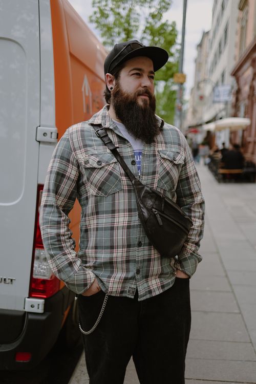 Free Man in checkered shirt and cap stands confidently by delivery van on city street Stock Photo