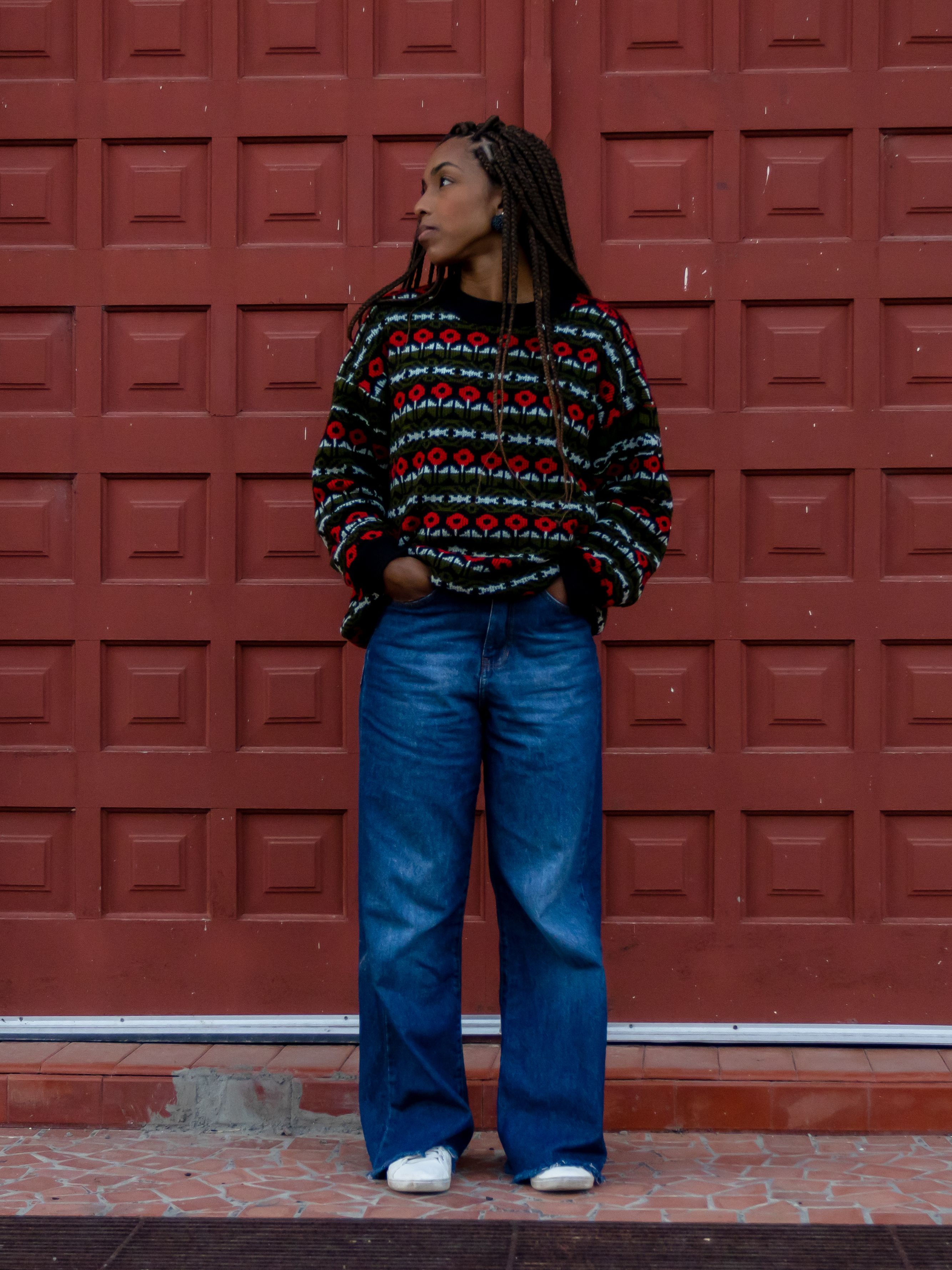 African American woman in a chic outfit stands confidently in front of a textured red wall in Urubici, Brazil.