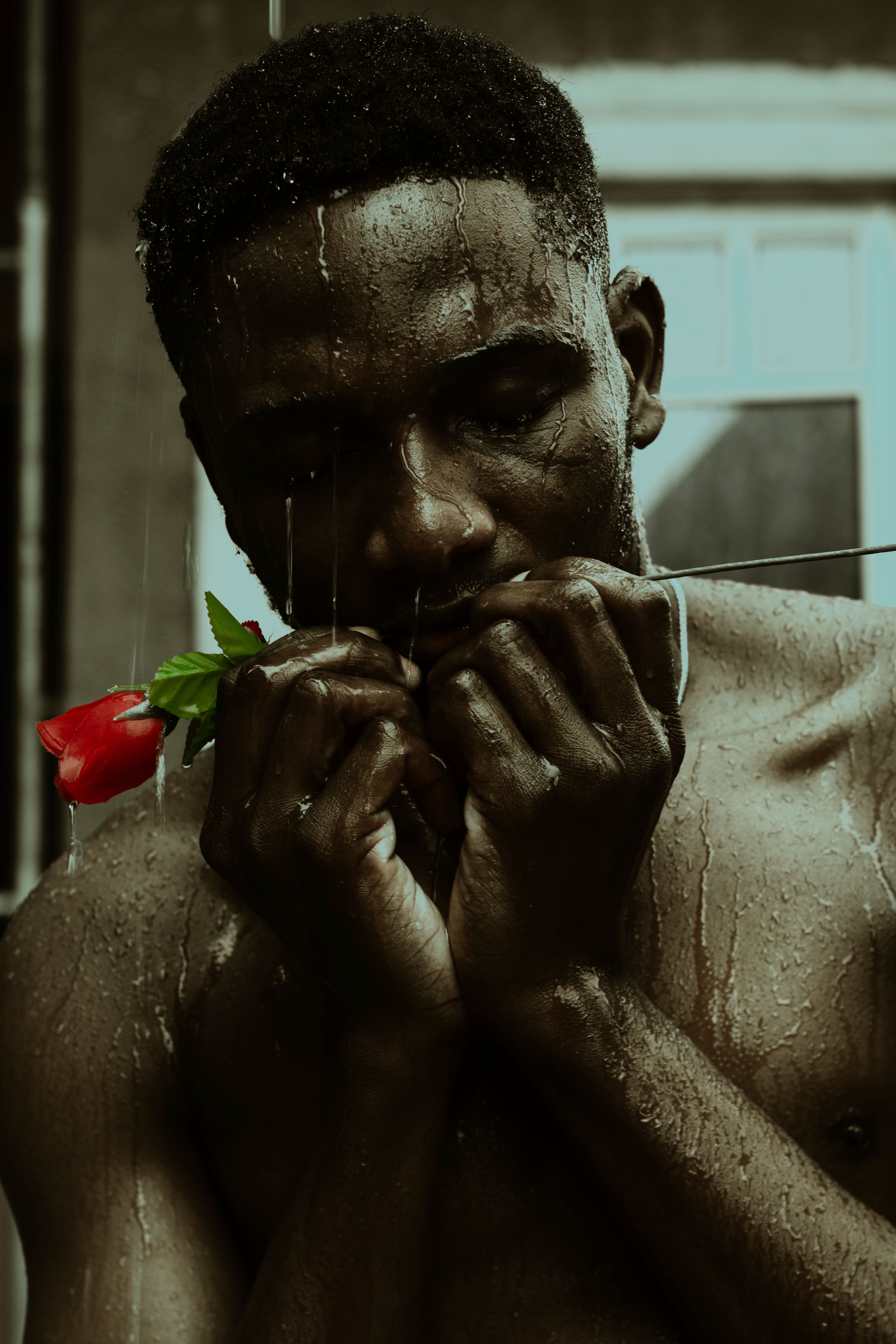 Emotional portrait of a man with a rose in a rain-soaked setting.