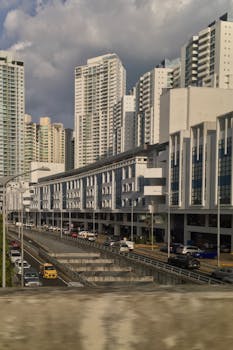 A bustling city street with modern skyscrapers and vibrant traffic under cloudy skies.