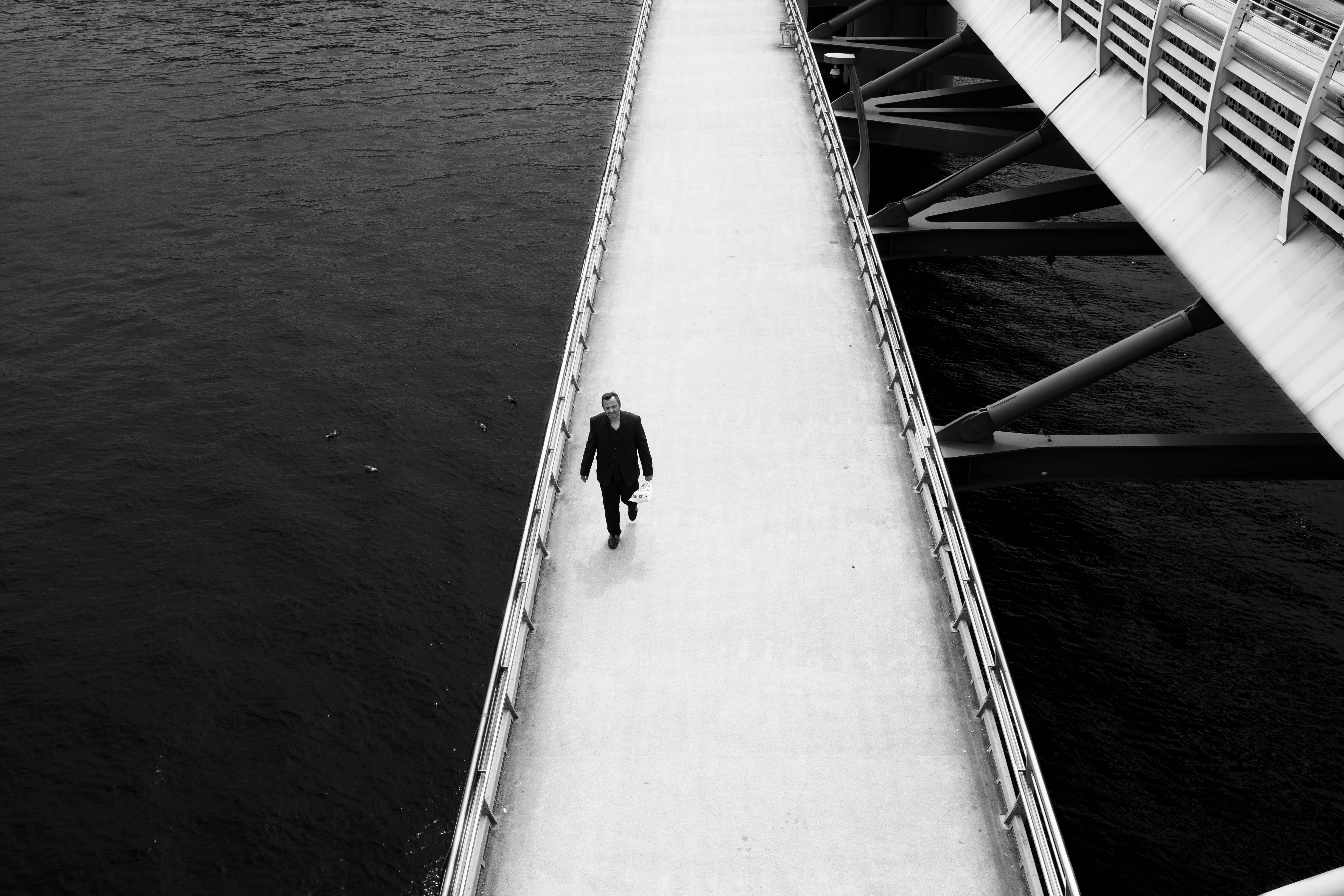 A lone figure walks across a black and white bridge over water in İstanbul.