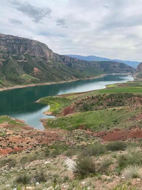 Free A tranquil river meanders through a lush valley under a cloudy sky, surrounded by green hills and rocky formations. Stock Photo