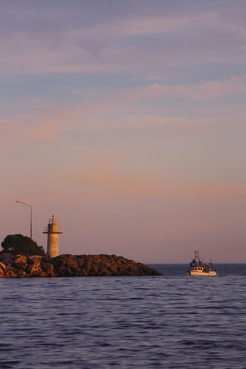 Free Serene coastal scene featuring a lighthouse and boat at sunset. Stock Photo