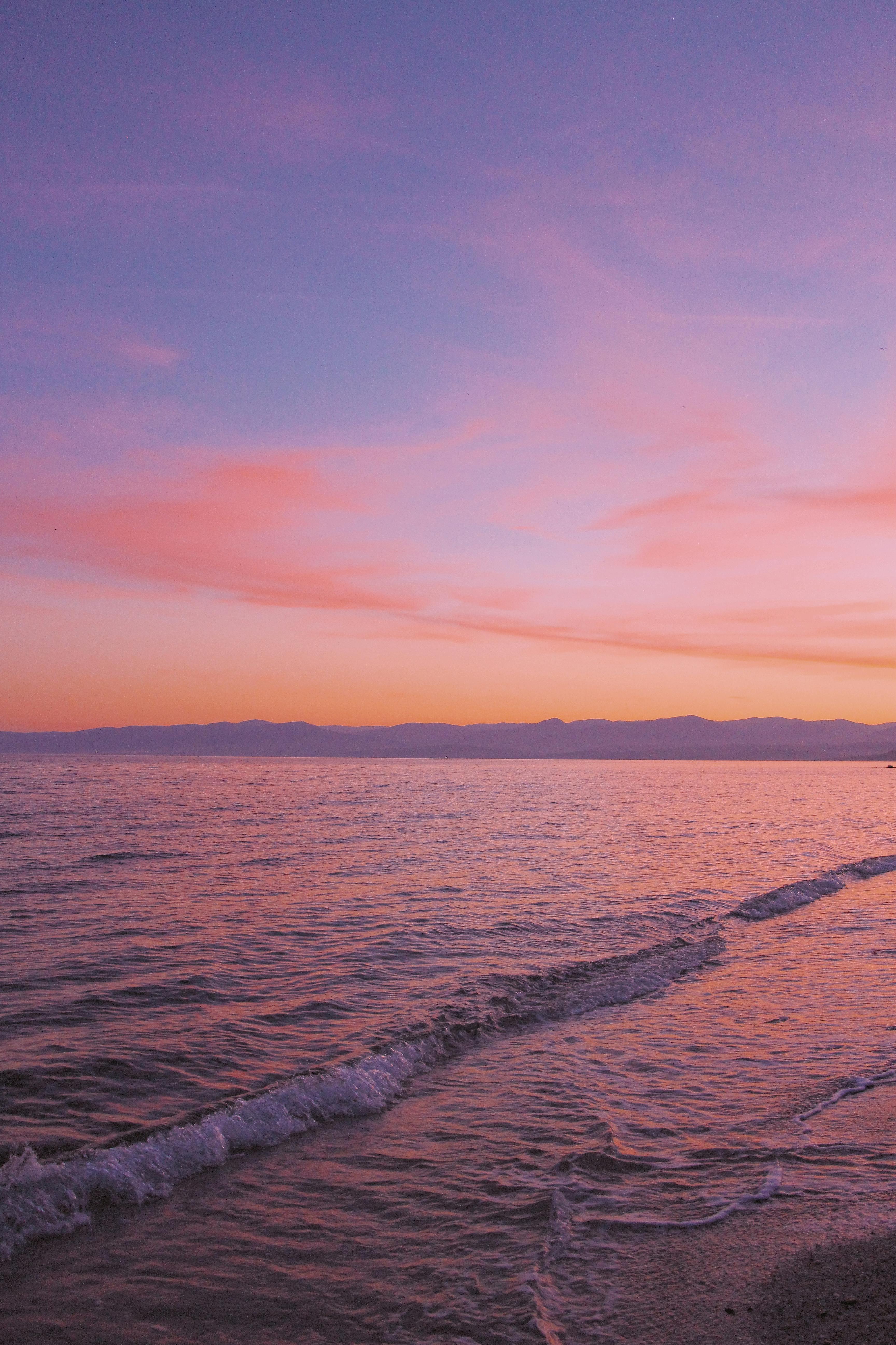 Tranquil waves gently lapping at the shore during a serene sunset, casting warm hues across the ocean.