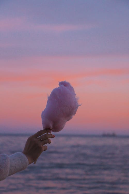 A Hand Holding Cotton Candy Against Sunset Sky