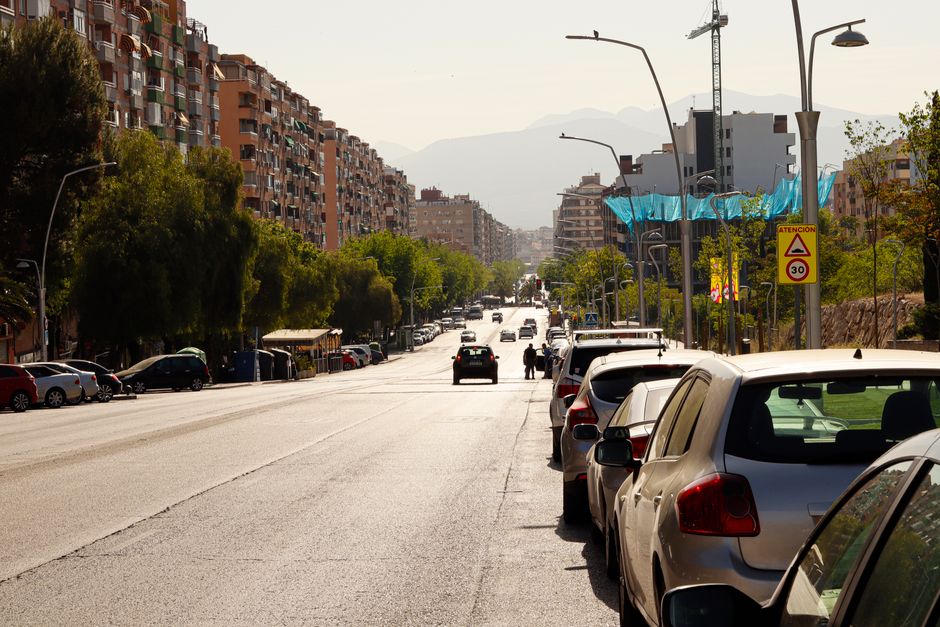 Vista de una calle de la ciudad con edificios residenciales, coches aparcados y tráfico ligero en un día soleado.