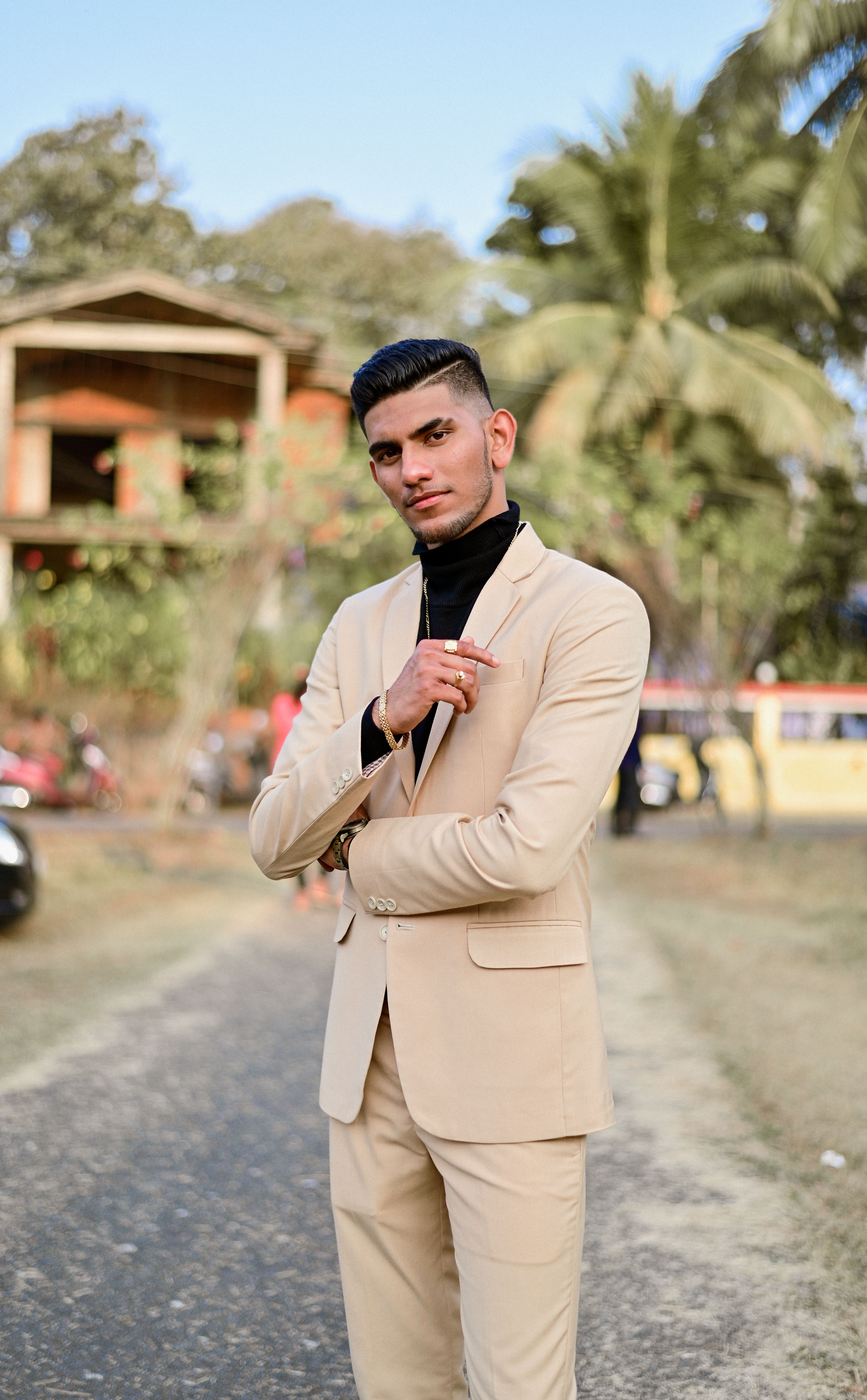 Fashionable man in a beige suit poses confidently outdoors with a tropical backdrop.