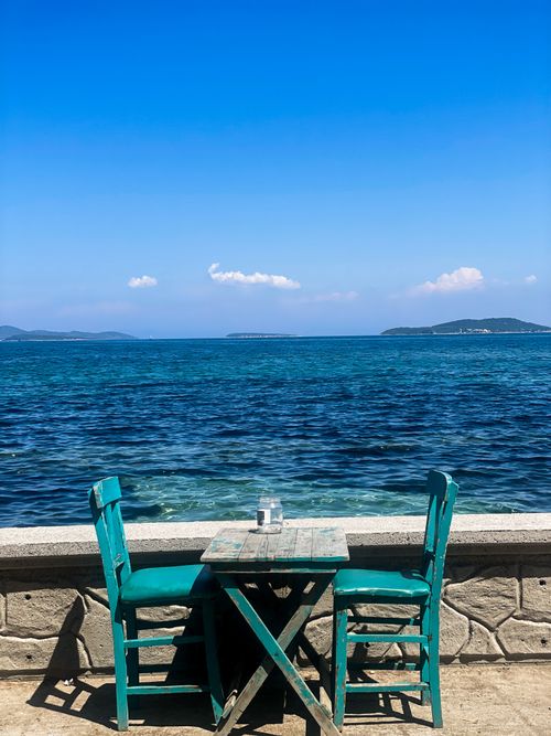 Free A serene seaside table setup with turquoise chairs by the azure Aegean Sea in İzmir. Stock Photo