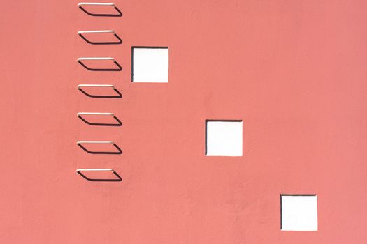 Minimalist pink building facade featuring a stark white ladder and geometric windows.